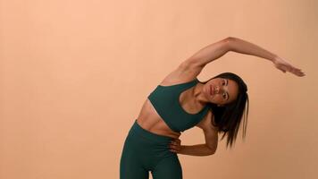 A young African American woman performs a dynamic stretch to maintain her fitness. She radiates health and energy in a sporty outfit against a soft, neutral backdrop. video