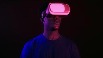 A confident millennial man with a cool style is immersed in virtual reality. Wearing a headset, he smiles as he experiences a vibrant, futuristic environment with neon lights. video