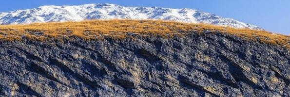 Rugged mountain landscape with snow-capped peaks and rocky cliffs under blue sky photo