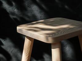 A Minimalist Wooden Stool Bathed in Sunlight Against a Dark Background, showcasing its natural grain and texture, a piece of simple elegant furniture photo