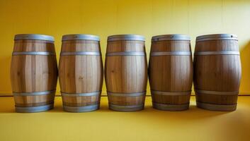 Wooden barrels with a natural, aged finish are lined up in front of a bright yellow backdrop, radiating a rustic and countryside feel. photo