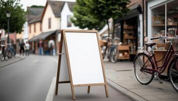 On a tranquil small-town street, a blank sandwich board catches the eye. Nearby, a craft store, bicycles, and trees add to the idyllic setting, with distant figures. photo