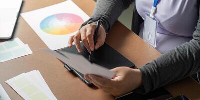 Graphic designer sketching ideas on a tablet while examining color palettes at her desk photo