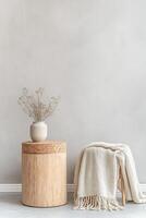 This setup presents a cork stool alongside a small bamboo table, adorned with a neutral throw blanket and a delicate potted plant, against a muted gray backdrop. Ample space invites creativity photo