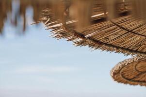 Simple straw beach umbrellas casting shadows on the sand with the Aegean Sea beyond. photo