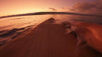 Surfer paddles on surfboard and duck dive under waves in ocean. First-person view and crashing waves with bright sunset video