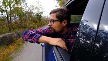 Closeup face of young man traveling by car while road trip. hipster pulling his face and hands out of car window and enjoying speed. Concept of freedom. video