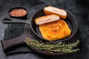 Fried cordon bleu cutlet with cheese and ham in pan. black background. top view photo