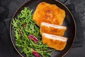 Chicken cordon bleu cutlet with cheese and ham on plate with salad. black background. top view photo