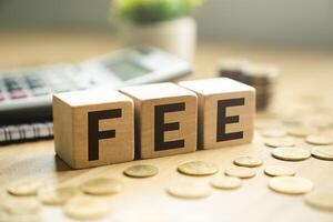 Wooden blocks spelling FEE placed on a desk with coins, calculator, and notebook, representing business fees, financial costs, transaction charges, accounting expenses, and economic budgeting photo