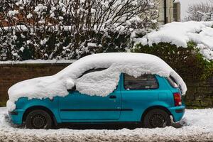Snow-Covered Teal Hatchback Parked on Snowy Street in Harrogate, UK. photo