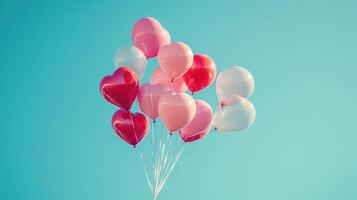 A Colorful Cluster of Heart-Shaped Balloons in Shades of Red and Pink Against a Clear Blue Sky Ideal for Celebrations, Events, and Romantic Occasions photo