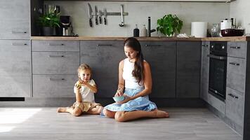 Mother and daughter sitting on kitchen floor, eating or having a breakfast and playing. Family bonding. High quality 4k footage video