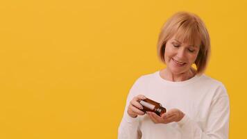 A cheerful woman with short hair holds a bottle of vitamins in one hand while gesturing with the other. The bright yellow background adds a lively touch to her expression of joy and curiosity. video