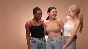 Three diverse women stand close together, sharing a joyful laugh. They are dressed casually in tank tops and jeans, creating a lighthearted atmosphere with their expressions and gestures. video