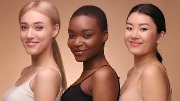 Three women of different backgrounds stand side by side, each smiling and showcasing their confidence. The background is a soft, neutral tone, emphasizing their diversity and beauty. video