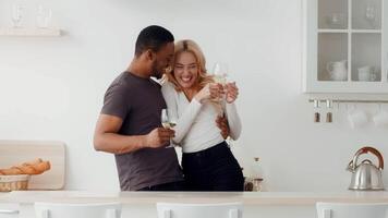 A joyful biracial couple shares a tender moment in their modern home. They toast with glasses of wine, smiling and embracing, showcasing their love and connection in a cozy atmosphere. video
