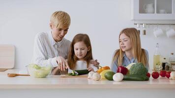 A parent is teaching two young children to prepare a healthy meal in a modern kitchen filled with fresh vegetables. Laughter and joy fill the space as they bond over cooking. video
