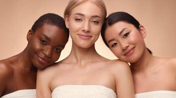 Three women of different backgrounds stand close, smiling warmly. They showcase diverse beauty while wearing simple white tops, creating a harmonious image of friendship. video