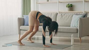 A woman practices athletic exercises on a yoga mat in a cozy living room. She focuses on her form while engaging in a physical fitness routine to maintain a healthy lifestyle. video