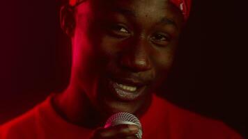 A stylish African American man smiles confidently while holding a microphone. He is surrounded by vibrant neon colors, creating a modern and energetic atmosphere. video