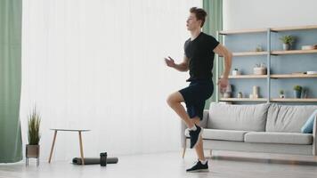 A sporty young man exercises indoors, focusing on a fitness routine in a well-lit living room. He maintains a healthy lifestyle while enjoying a comfortable environment. video