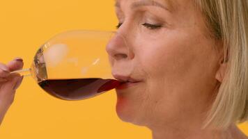 A woman enjoys a glass of red wine, appreciating its aroma and flavor. The bright yellow background creates a lively and warm atmosphere, enhancing her moment of relaxation. video