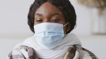 An African American woman sits at home, wearing masks and wrapped in blankets, as she cope with symptoms of flu and cold. video