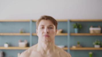 A sporty young man exercises in a well-lit home environment, showcasing his athletic build. He performs a challenging workout routine that emphasizes fitness and health. video