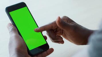A young African American man focuses on a smartphone display, tapping the screen with his finger. The ambiance suggests a comfortable home environment, highlighting technology use. video