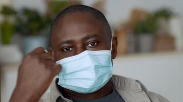 In a well-lit room, a young African American man is focused on his gadget while adjusting his face mask. He appears engaged and surrounded by contemporary decorations. video