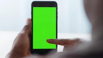 A young African American man interacts with a smartphone while sitting at home. The device displays a blank green screen, highlighting his focus on technology and digital connectivity. video