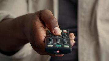 A young African American man relaxes in his home, focused on the remote in hand, surrounded by gadgets and modern tech, showcasing typical technology use, cropped video