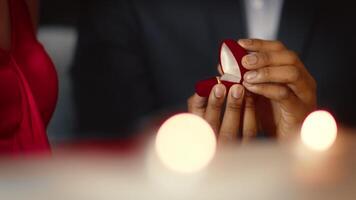 A diverse couple enjoys an intimate dinner at a cozy restaurant. One partner presents a ring from a red ring box, creating a heartfelt and memorable moment filled with love and affection. video
