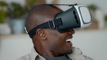 A joyful millennial man engages with virtual reality technology, laughing and immersed in an interactive experience at his home. Modern gadgets surround him, highlighting his tech-focused lifestyle. video