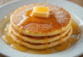 Stack of pancakes with melting butter, powdered sugar, and drizzled syrup on a decorative white plate. Close-up food photography for breakfast design and print. photo