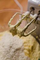 Close-up of hand mixer beaters covered in creamy cake batter in kitchen table . High quality photo