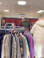 Thrift store shoppers browse racks of clothing. High quality photo