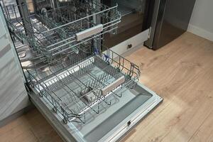 Open empty dishwasher with empty racks and extended basket in modern kitchen ready for loading. Home appliance photo