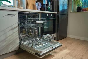 Open empty dishwasher with empty racks and extended basket in modern kitchen ready for loading. Home appliance photo