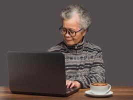 An elderly Asian woman with short grey hair uses a laptop to search for data from the internet while sitting at the table photo