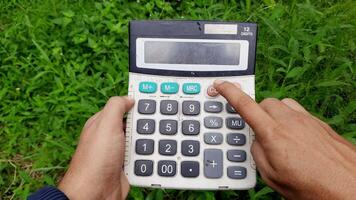 Person using an old calculator outdoors in a grassy area while pressing the clear button video