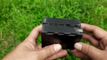 Footage showing a lithium multifunction battery being held by a person against a backdrop of green grass. video