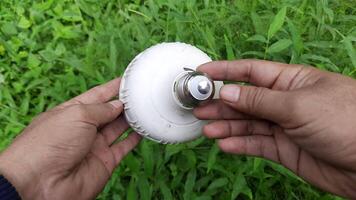 A white plastic shell of an LED light being held by a person, set against a lush green grass background video