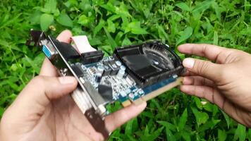 A person holds an old graphic card in their hands while surrounded by lush green plants video