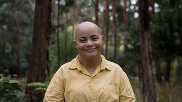 Photo of bald woman with Down syndrome smiling against forest background, capture happiness and connection with nature. Community concept