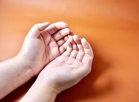 Hands with open palms praying and religious gesture pose isolated on horizontal orange brown terracotta colored background. photo