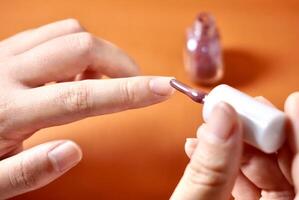 Hand applying nail polish on fingernail isolated on horizontal orange brown terracotta colored background. photo