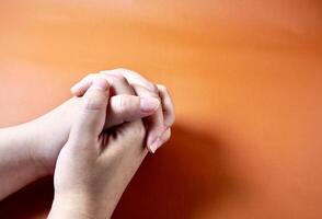 Clasped hands with praying and religious gesture pose isolated on horizontal orange brown terracotta colored background. photo