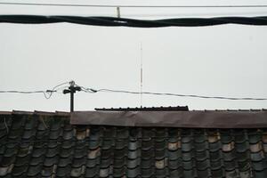 Rooftop With Antenna and Overhead Power Lines on a Cloudy Day photo